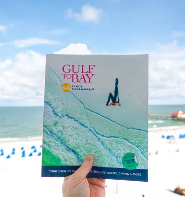a person holding up a Gulf to Bay magazine with Clearwater Beach and Pier 60 as the backdrop