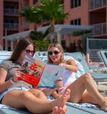 two women sitting in lounge chairs at the Hyatt Regency Clearwater Beach reading a Gulf to Bay Destination Magazine