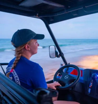 Woman driving an ATV on the beach during sunrise.