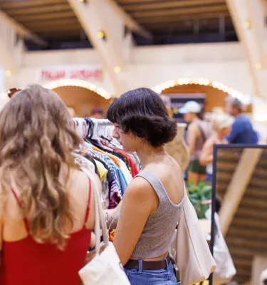 Women shopping at an indoor market looking at clothing racks.