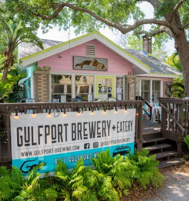 the exterior of the Gulfport Brewery with lush trees and greenery around it