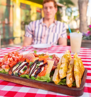 a man sits at a table outside that has bruschetta and other appetizers at Pia's in Gulfport