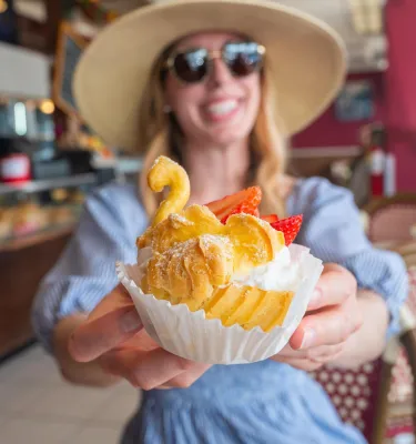 a smiling woman holding a swan-shaped croissant with berries and cream at Cafe de Paris Bakery in Indian Rocks Beach