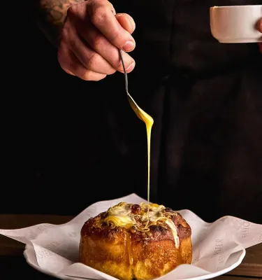 a chef drizzling a bechamel sauce on top of a popover