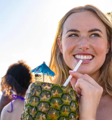 a young woman sips a drink from a pineapple while on the beach with friends in St. Pete-Clearwater