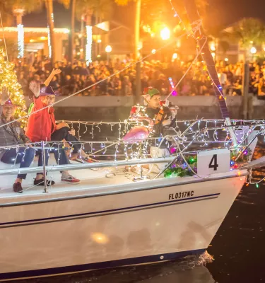 People waving on a sailboat wrapped in Christmas lights