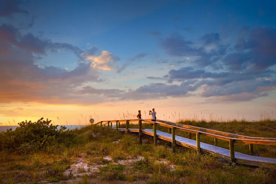 A couple taking photos during sunset at a beach walkway on beautiful Pass-a-Grille Beach near St. Pete Beach, Florida