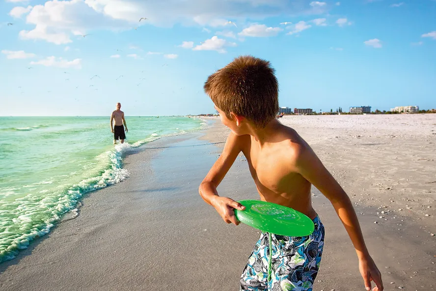 A boy playing frisbee with his dad in on the beach in Treasure Island near St. Pete Beach
