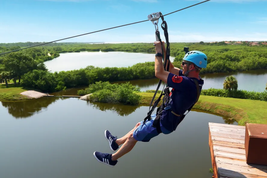 a man ziplines above Mobbly Bayou Wilderness Preserve in Oldsmar; a lake and trees can be seen below him