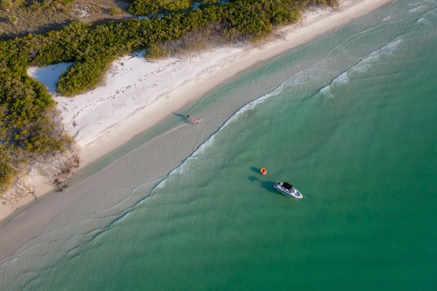 Aerial view of a boat anchored off the beach at Shell Key Preserve; dunes border the beach and the Gulf water is emerald green