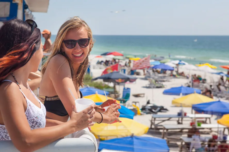 Zwei Frauen genießen Cocktails im zweiten Stock eines Caddy's Restaurants mit Blick auf den Strand