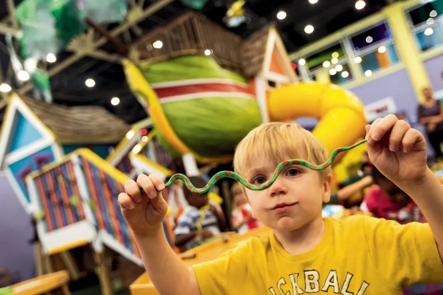 A child holds up a small toy snake at the Great Explorations Children's Museum