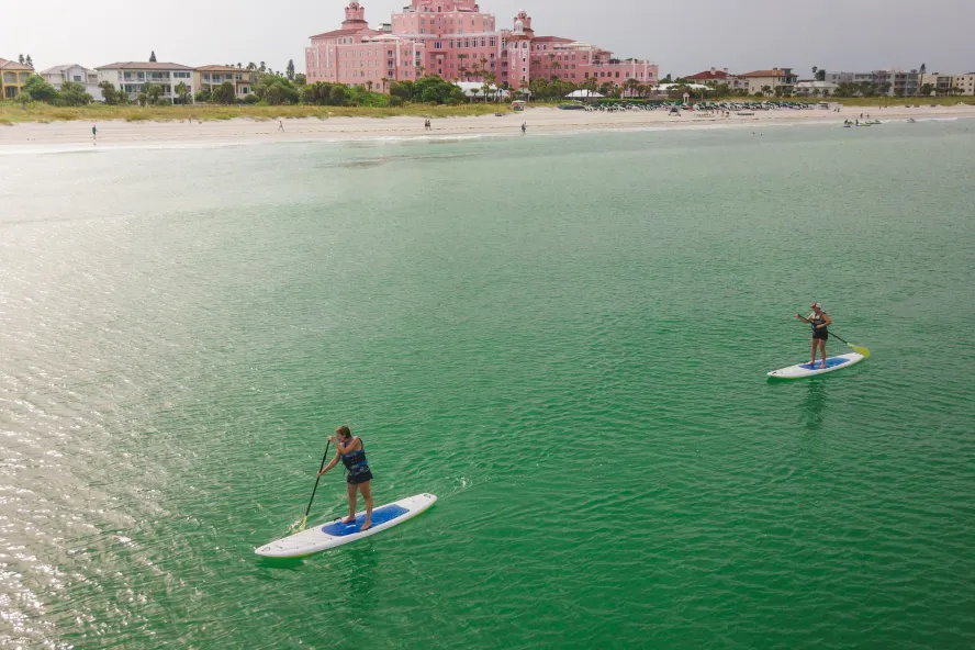 Two stand-up paddleboarders with the Don CeSar in the background