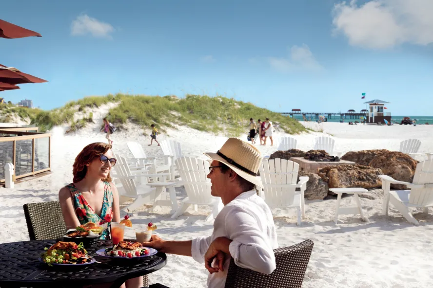 A couple enjoys cocktails on the beach at Tate Island Grill at the Sandpearl Resort