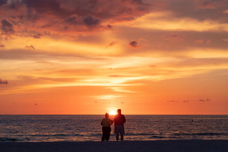 A couple stands on Pass-A-Grille Beach as the sun sets