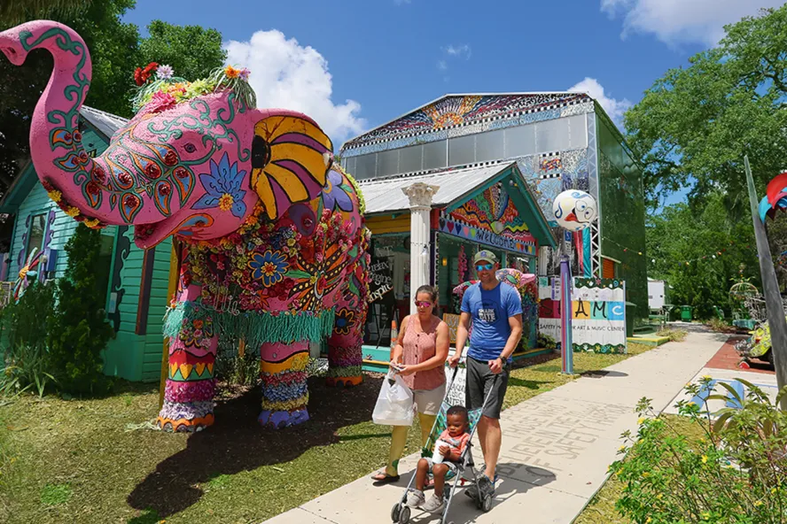A couple strolling with a child in front of the pink elephant in front of the Safety Harbor Art & Music Center