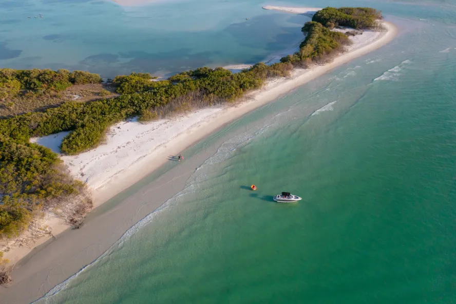 Luftaufnahme eines von grünem Wasser umgebenen Bootes und eines Familienspaziergangs am nahegelegenen, unberührten Strand