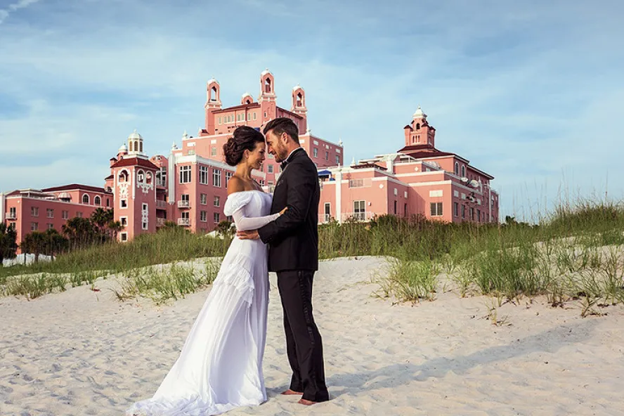 A couple hugging each other posing in front of Don Cesar for their wedding.