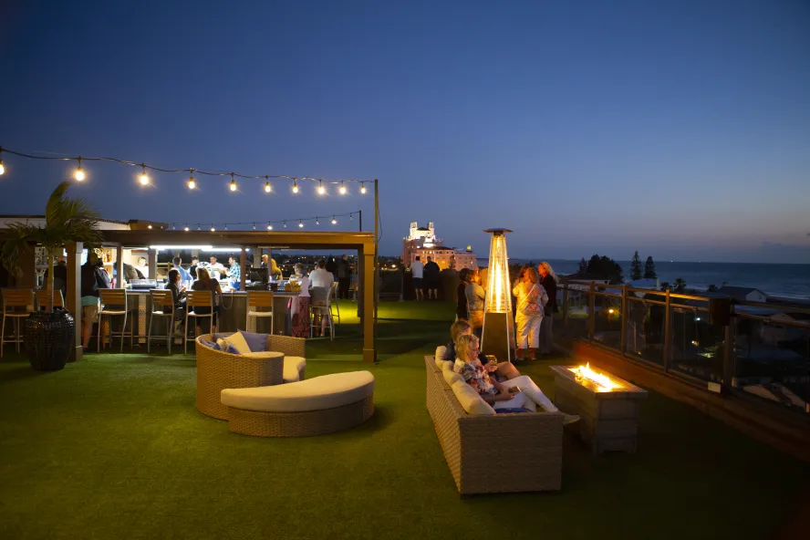 Overview of rooftop bar at Hotel Zamora at dusk showing people enjoying drinks by the fireplace.