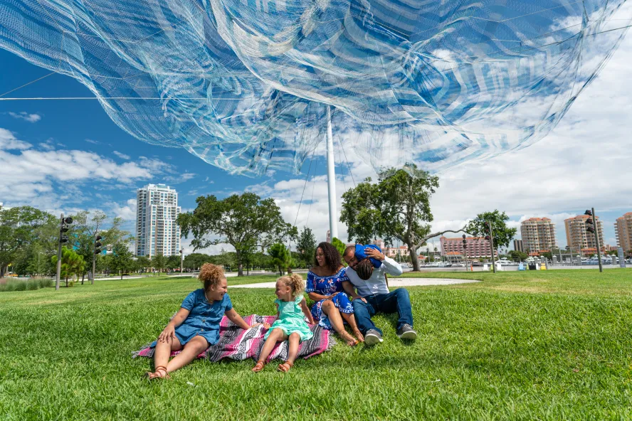 A family enjoying themselves in the grass field under the Echelman Sculpture at the St. Pete Pier.
