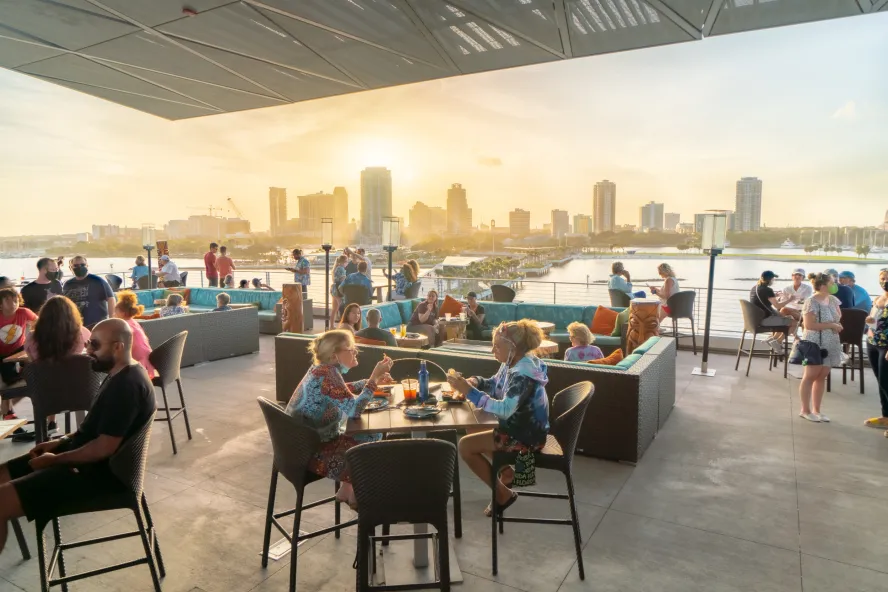 Several people enjoying drinks and meals while watching the sunset and St. Pete skyline from the rooftop of Pier Teaki.
