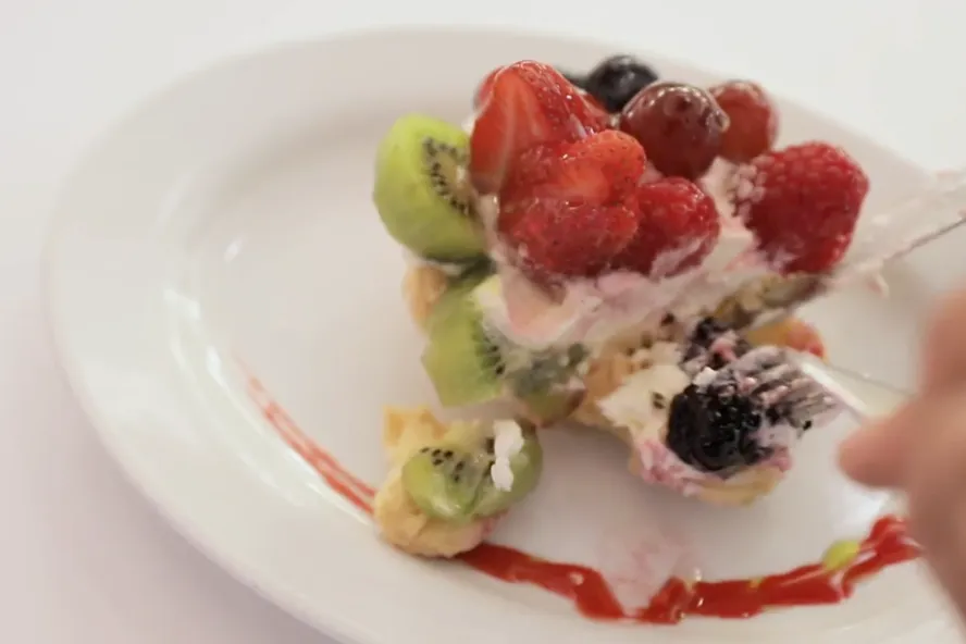 Eine Person schneidet ein Beeren-Kiwi-Dessert aus dem Hellas Restaurant