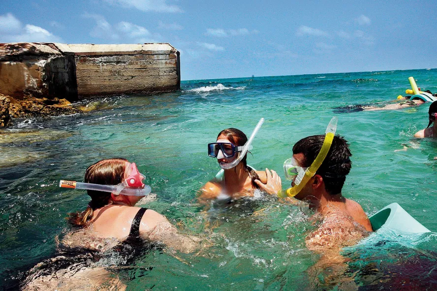 A group snorkeling in clear blue green water next to a fort.