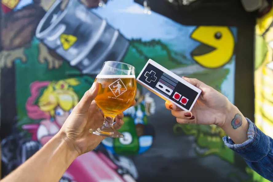 People Cheers a beer and a game controller outside the brewery Right Around the Corner in downtown St. Pete