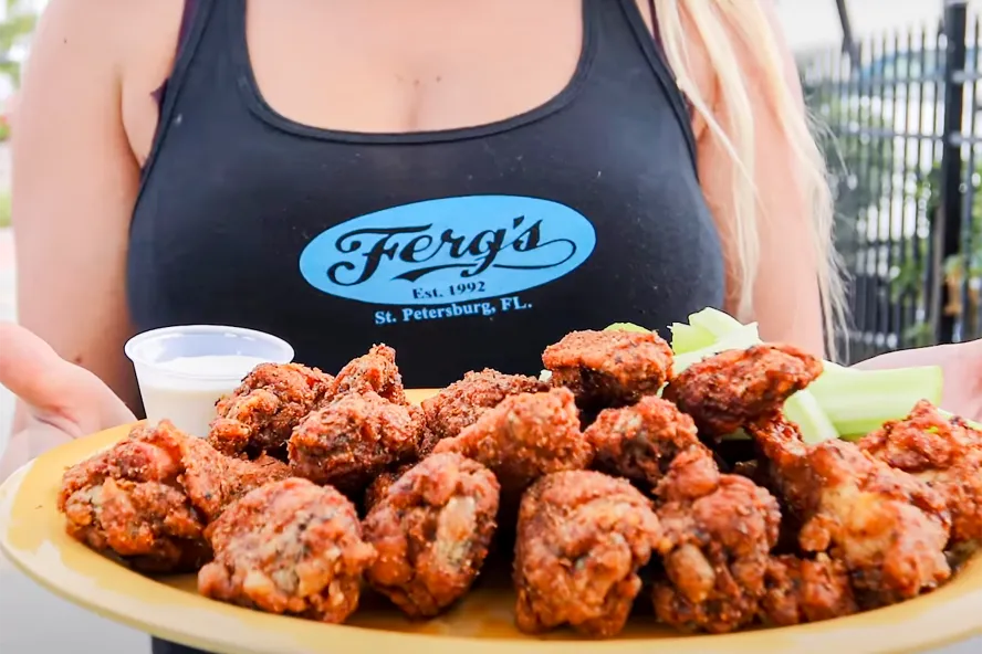A woman holds up a plate of chicken wings at Ferg's Sports Bar