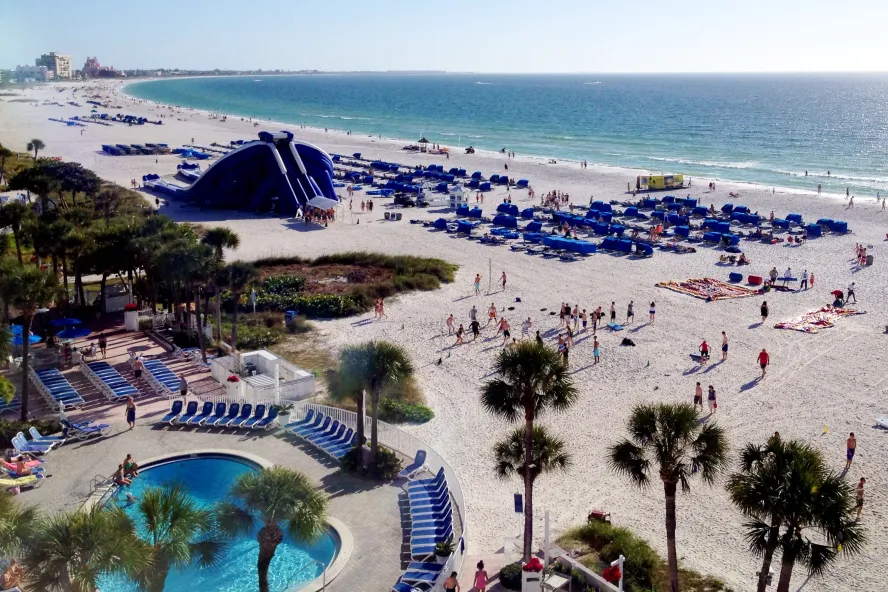 Arial view of Tradewinds Hotel Showing the pool by the beach, beach chairs lined on the beach and there iconic giant blowup slide.