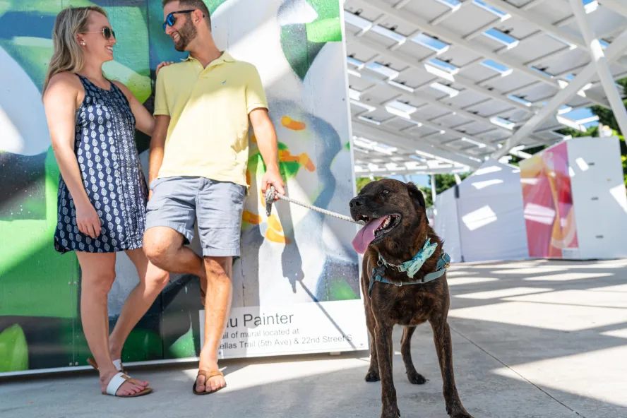 A couple hanging out against a mural with their large brown dog.