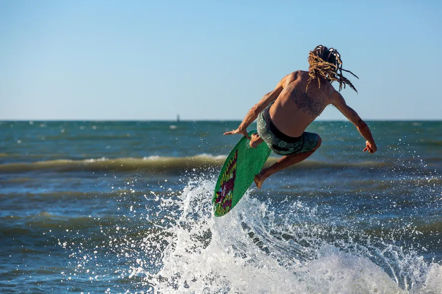 A man skimboards off the beach