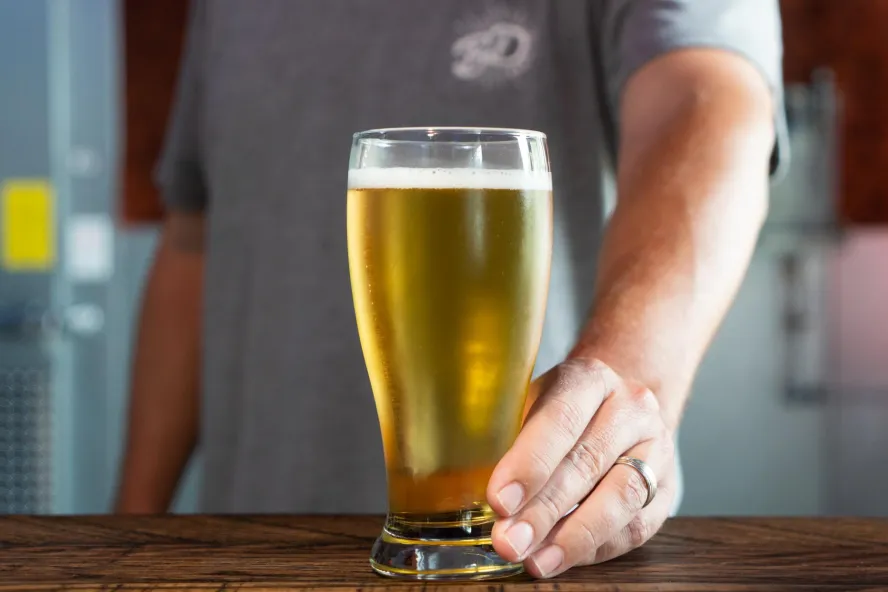 Fotografía de cerca de un camarero ofreciéndote un vaso de cerveza.