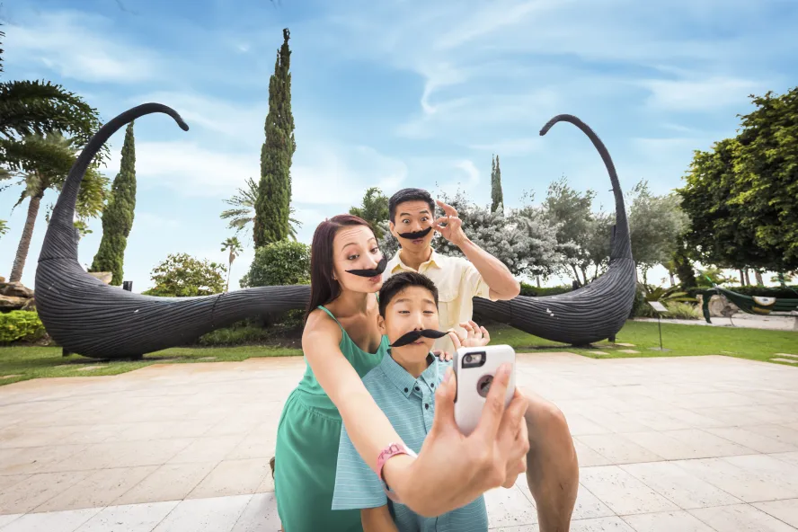 An Asiatic family wearing fake mustaches taking a selfie in front of the famous mustache sculpture at the Dali museum in St. Pete.