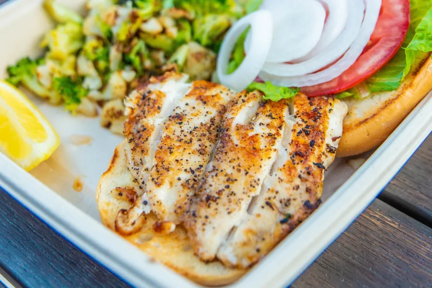 A close view of a grouper fish plate with onions, tomatoes and green vegetables.