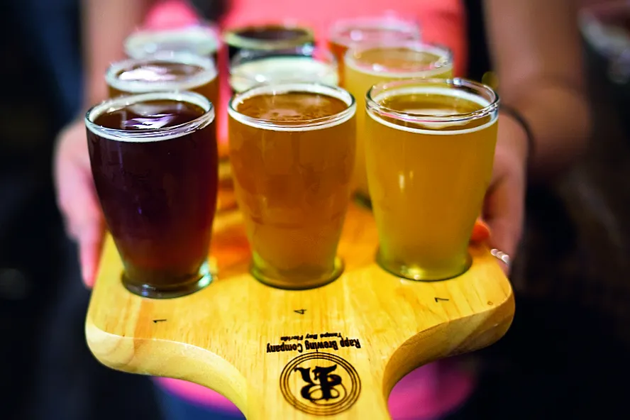 A lady wearing a pink shirt holding a beer sampler.