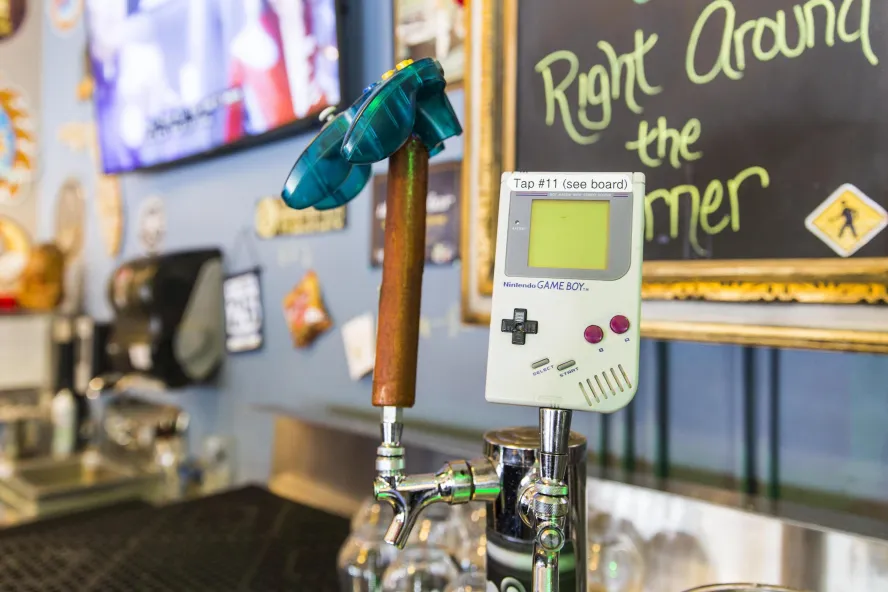 A close view of an old Nintendo Game Boy, with beer taps in the background.