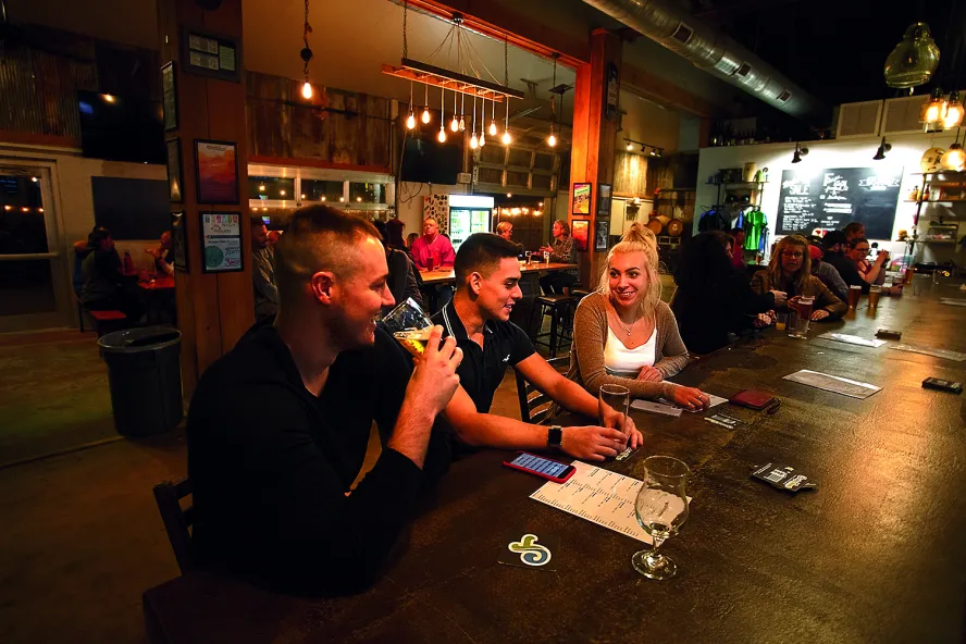 Three friends enjoying drinks at the bar at Crooked Thumb Brewery.