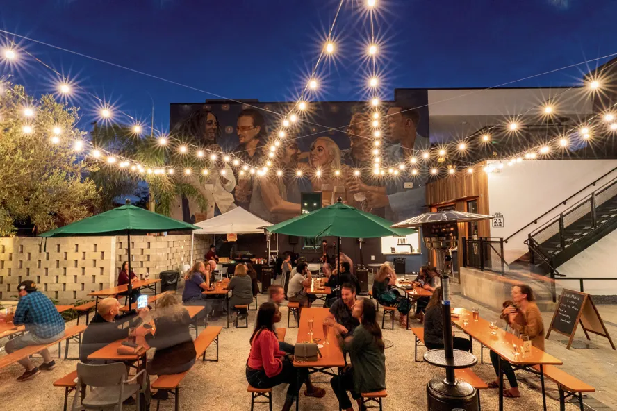 Several people enjoying drinks in the outdoor area of Grand Central Brew House at dusk.