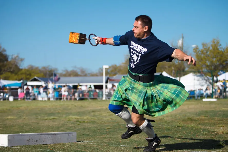 A man in a green kilt throws a weight competitively.