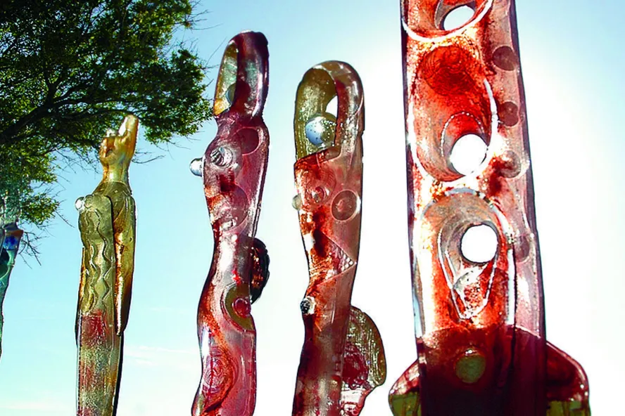 Five sculptures in a line next to a palm tree with the sunlight in the background.