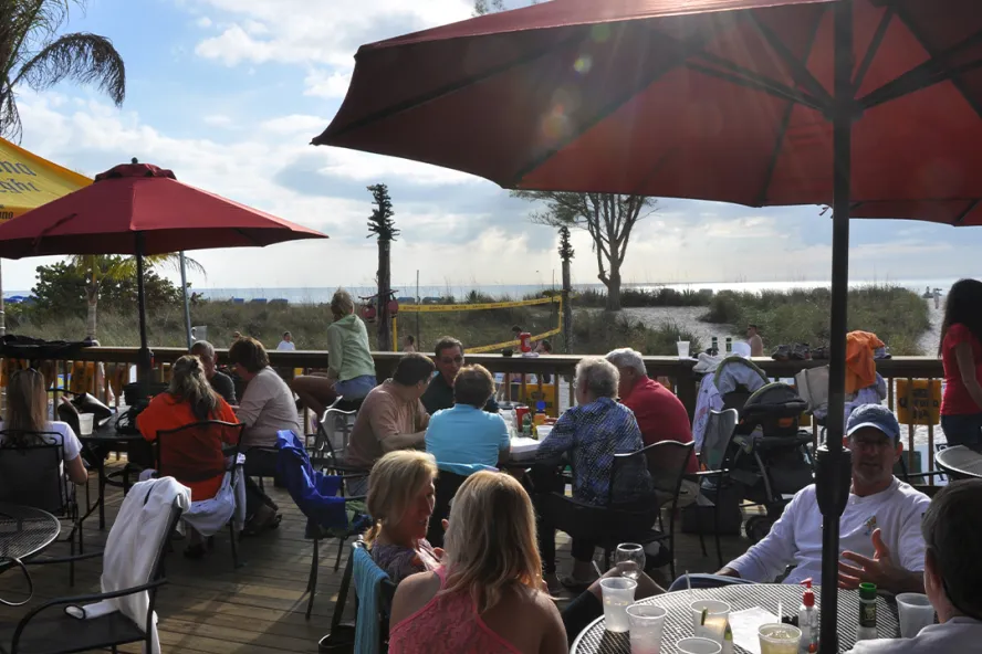 A large group of people at the outdoor area of a beachfront restaurant.