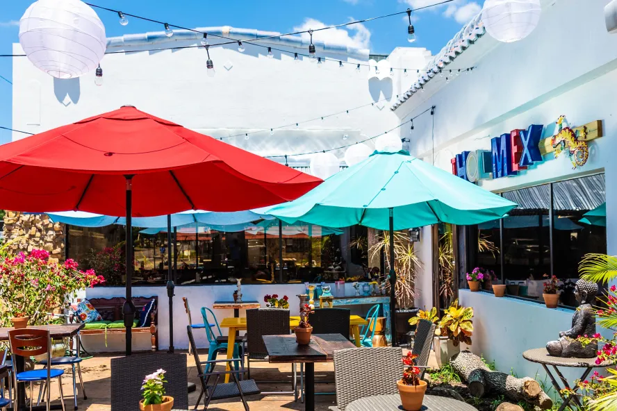 Outside photo of the patio seating area at Nitally's ThaiMex restaurant. Featuring red and blue umbrellas, white string lights and lots of outdoor plants.