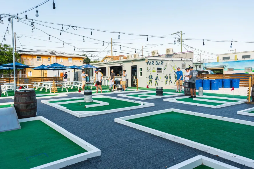 Outside image of mini-golf bar Par Bar, featuring various holes, string lights and giant beer pong.