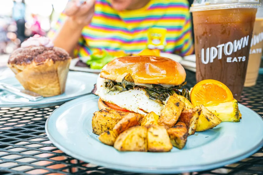 Food plates of an egg and spinach sandwich with roasted potatoes and a pastry.