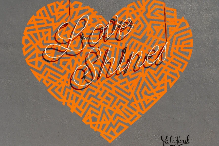 an orange heart-shape mural on a gray background says Love Shines in cursive script