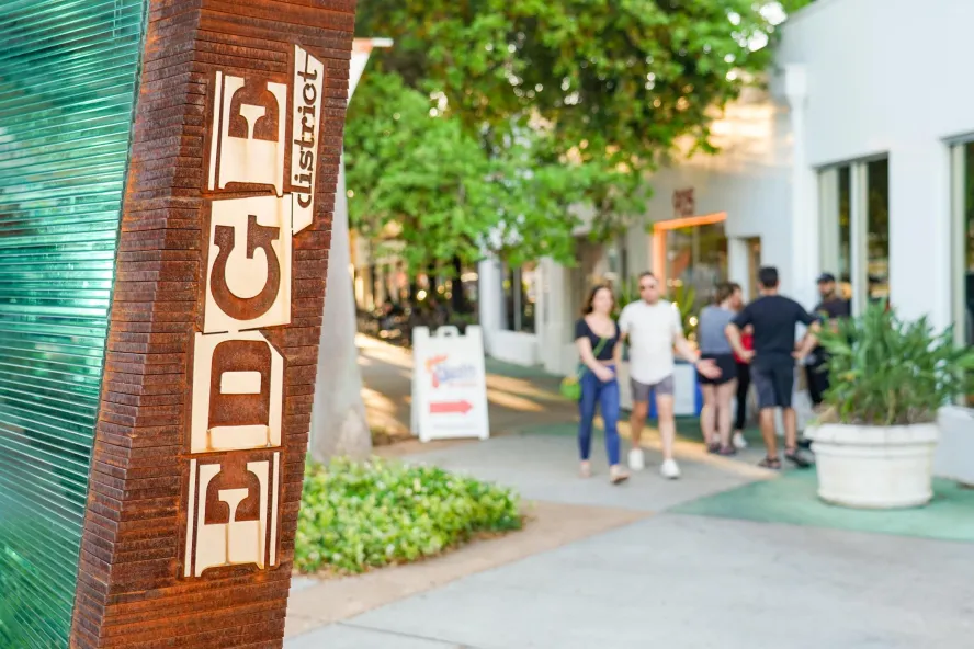 a decorative lettered sign for the EDGE district in St. Pete is in the left of the screen, with three people walking in front of a storefront on the right