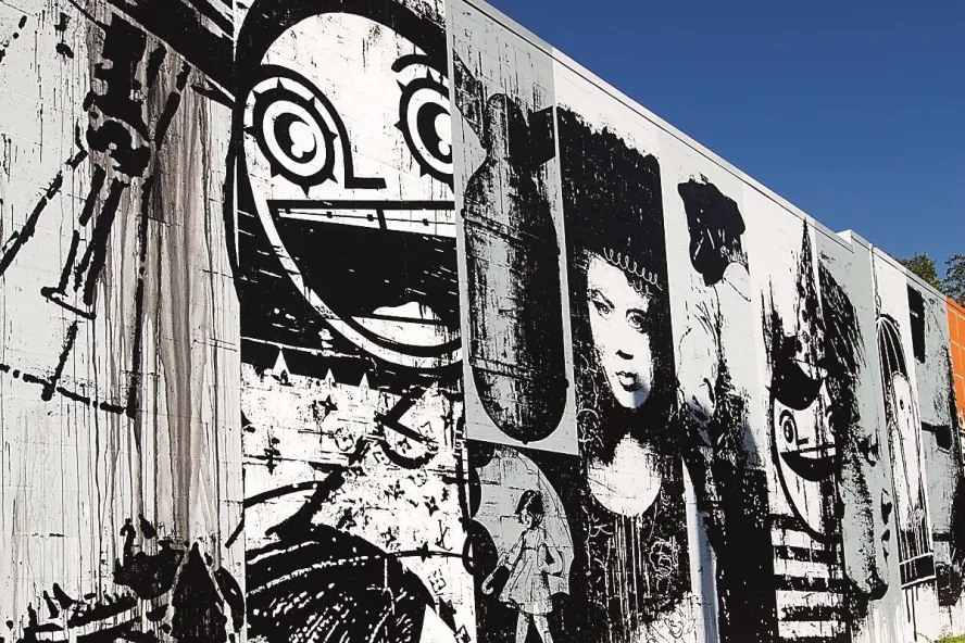 a graphic mural in black and white of many faces is on the side of a building with clear blue sky above
