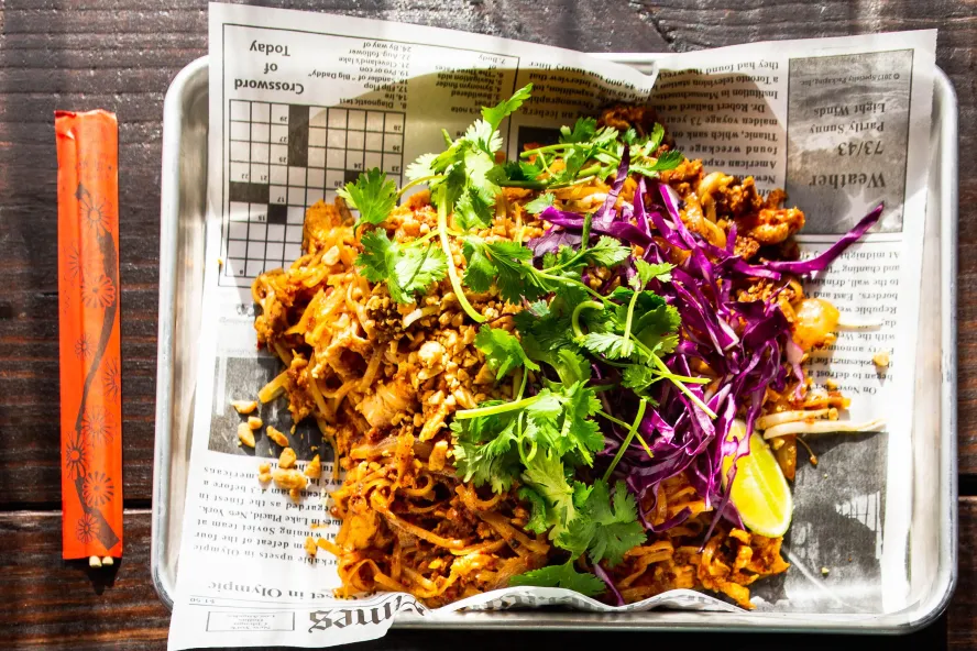 a plate of shredded pork or chicken decorated with cilantro and served on newspaper