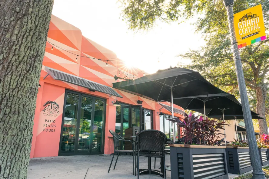 Exterior shot of Wild Child restaurant featuring decorated pink walls, black outside seating and trees.